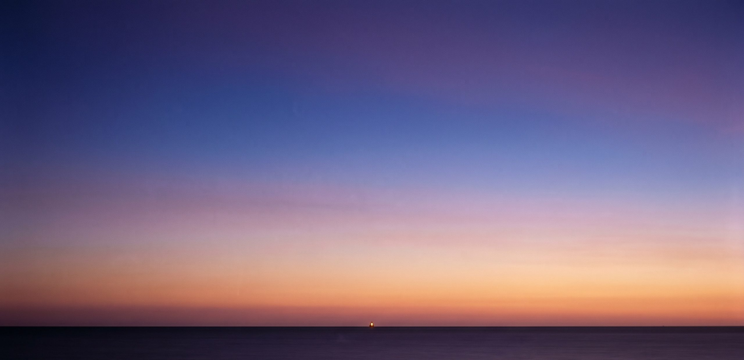 A pastel-colored horizon over a calm sea at dusk, a single small warm light just above the waterline.