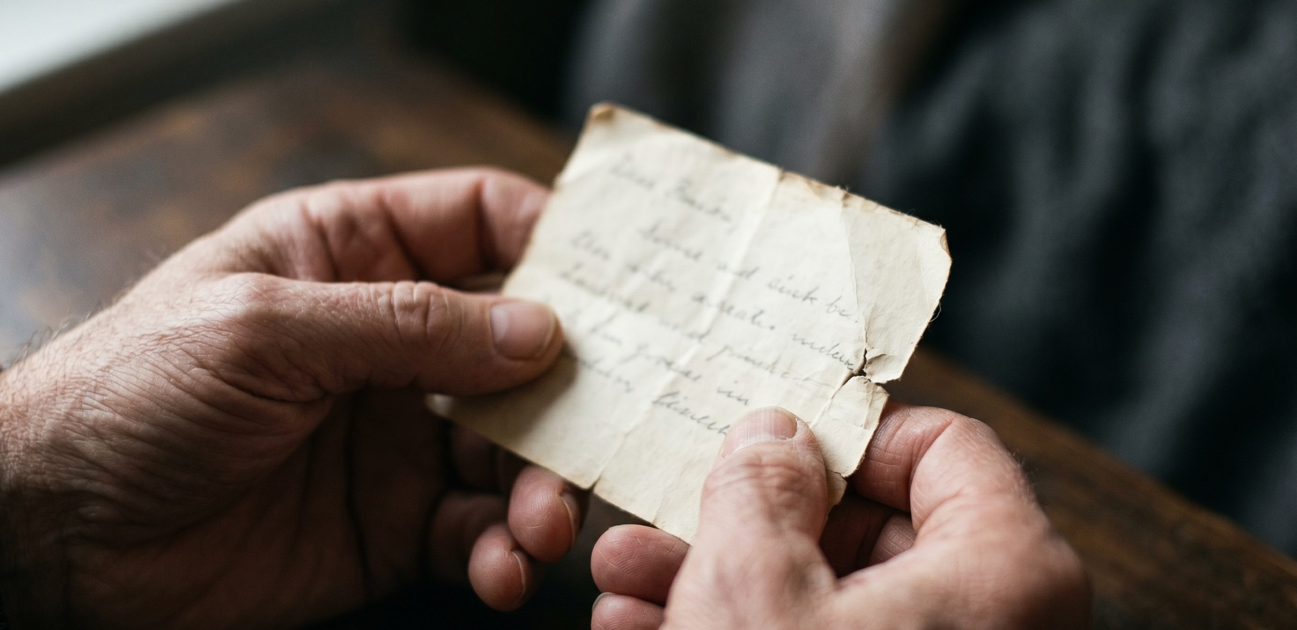 Older hands holding a small worn handwritten note in soft window light.