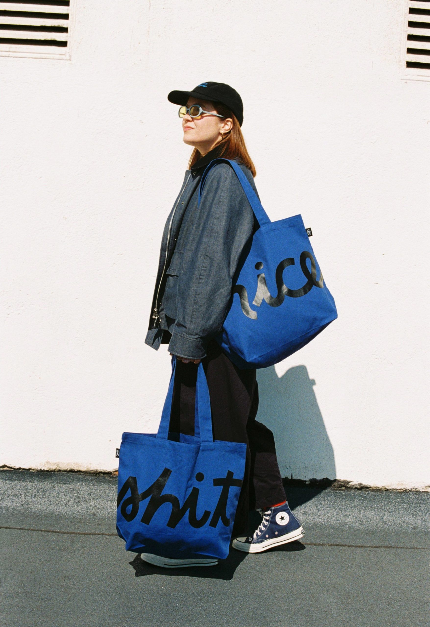 A person carrying two blue Niceshit tote bags reading nice and shit.