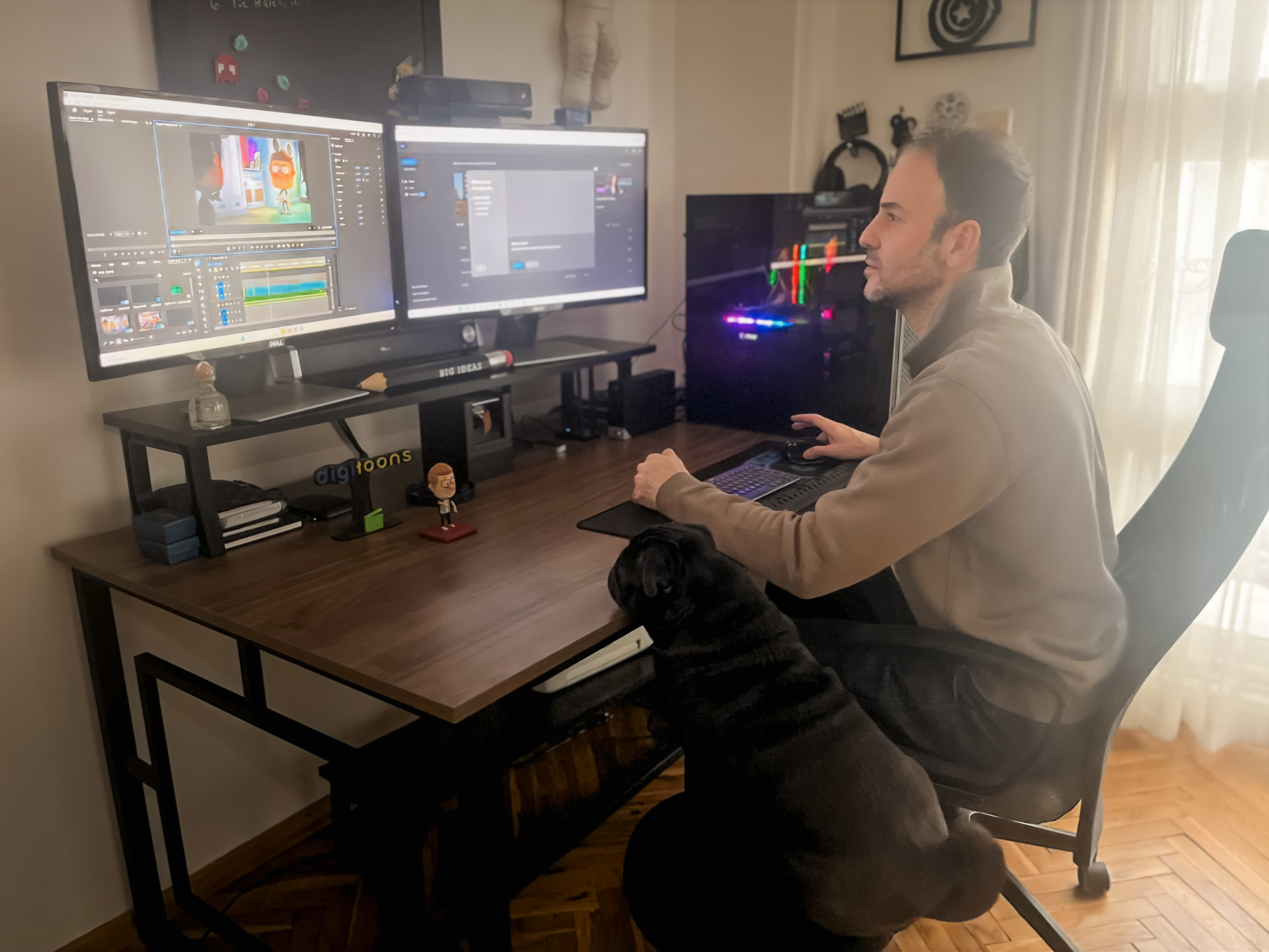 Wide view of Serhan Yorganci's dual-monitor setup with an editing timeline on screen, the black pug sitting beside his chair